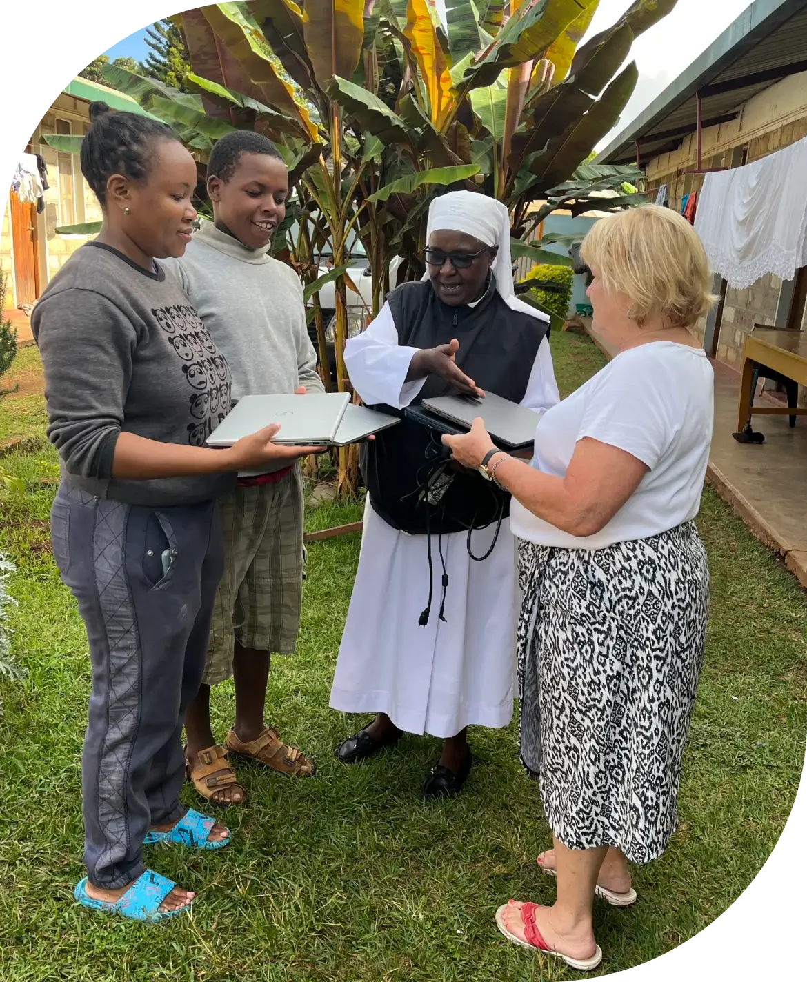 Volunteers presenting laptops to local students outdoors