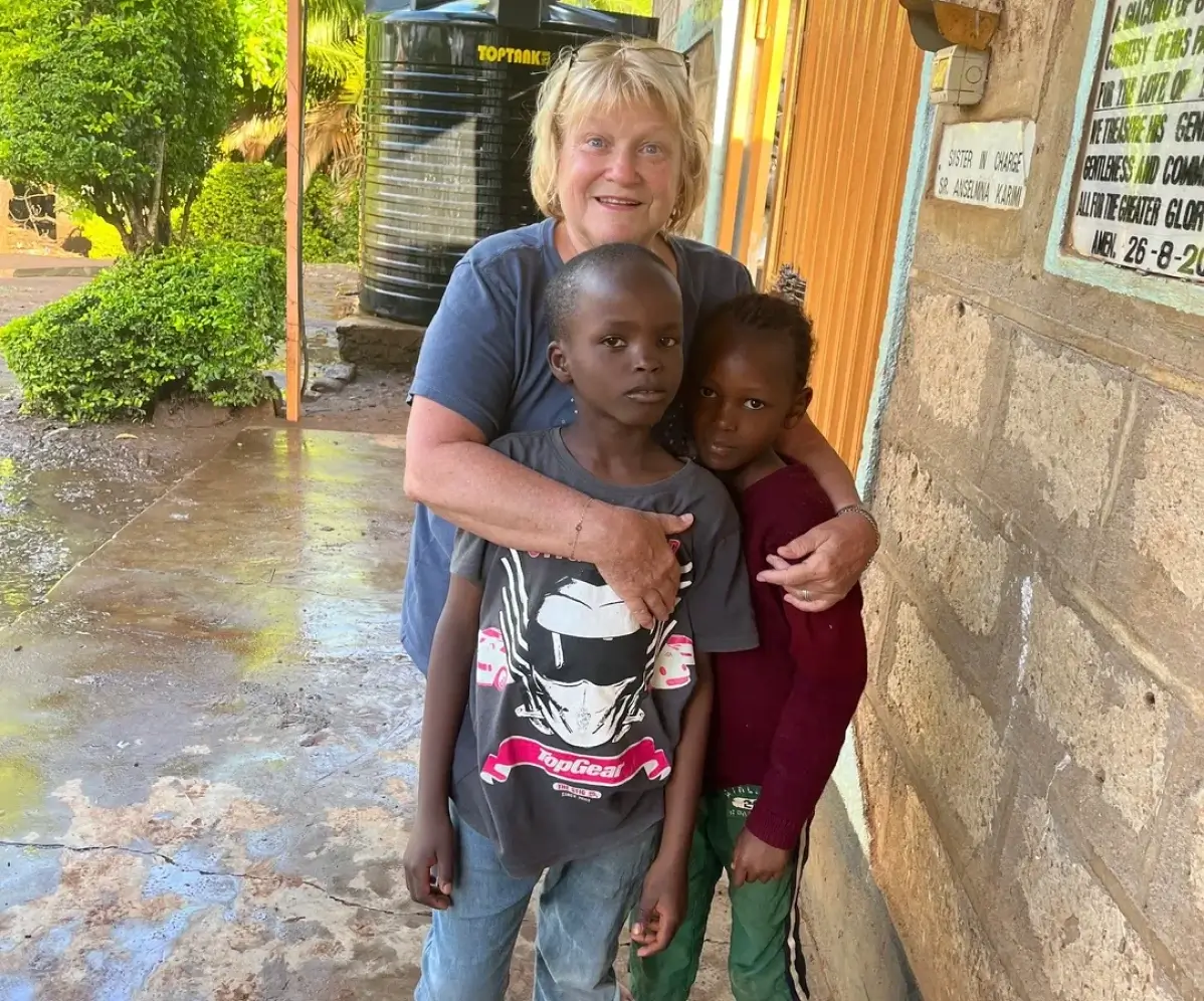 Volunteer hugging two children by wall