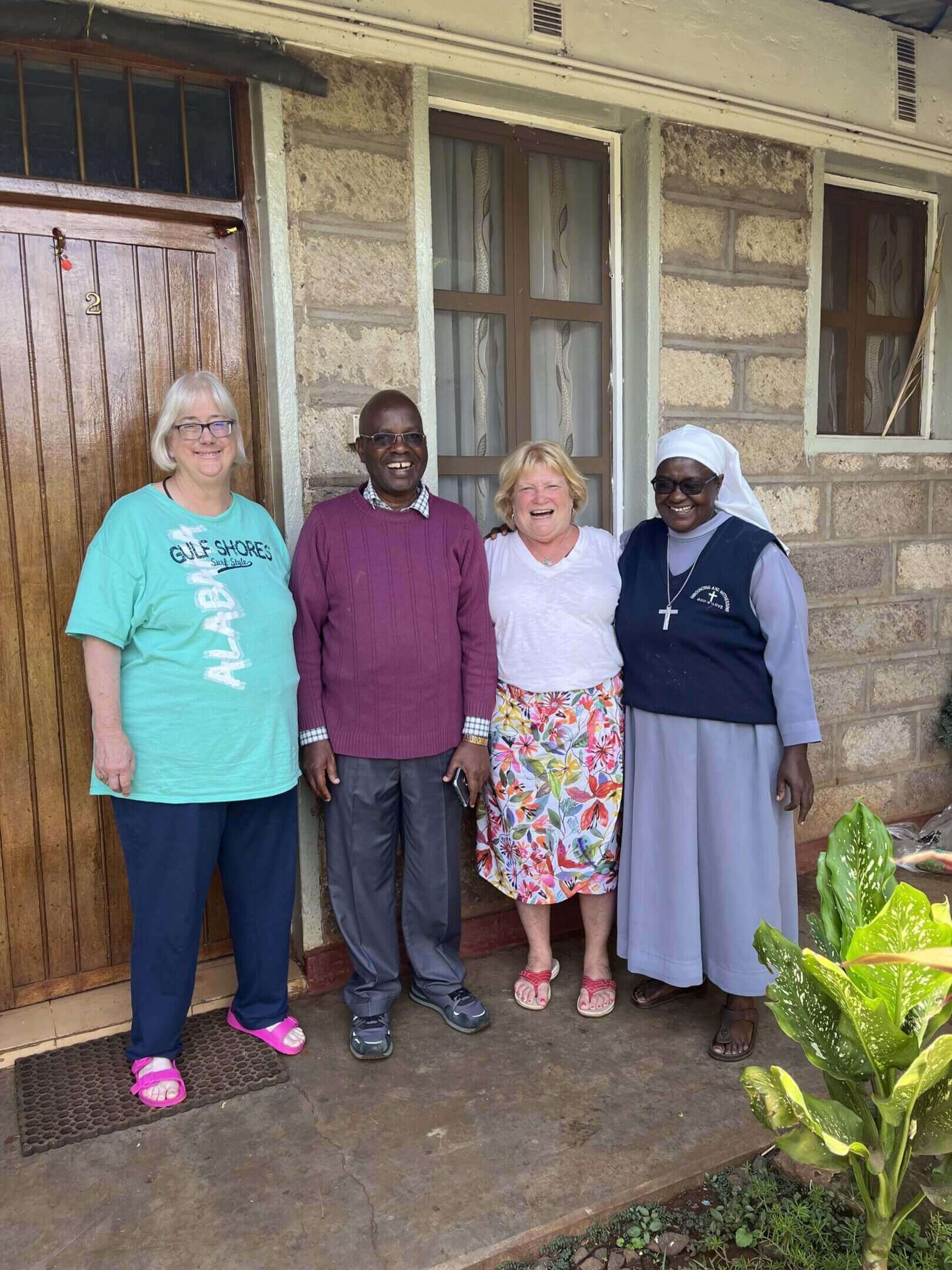 Four people smiling in front of house.