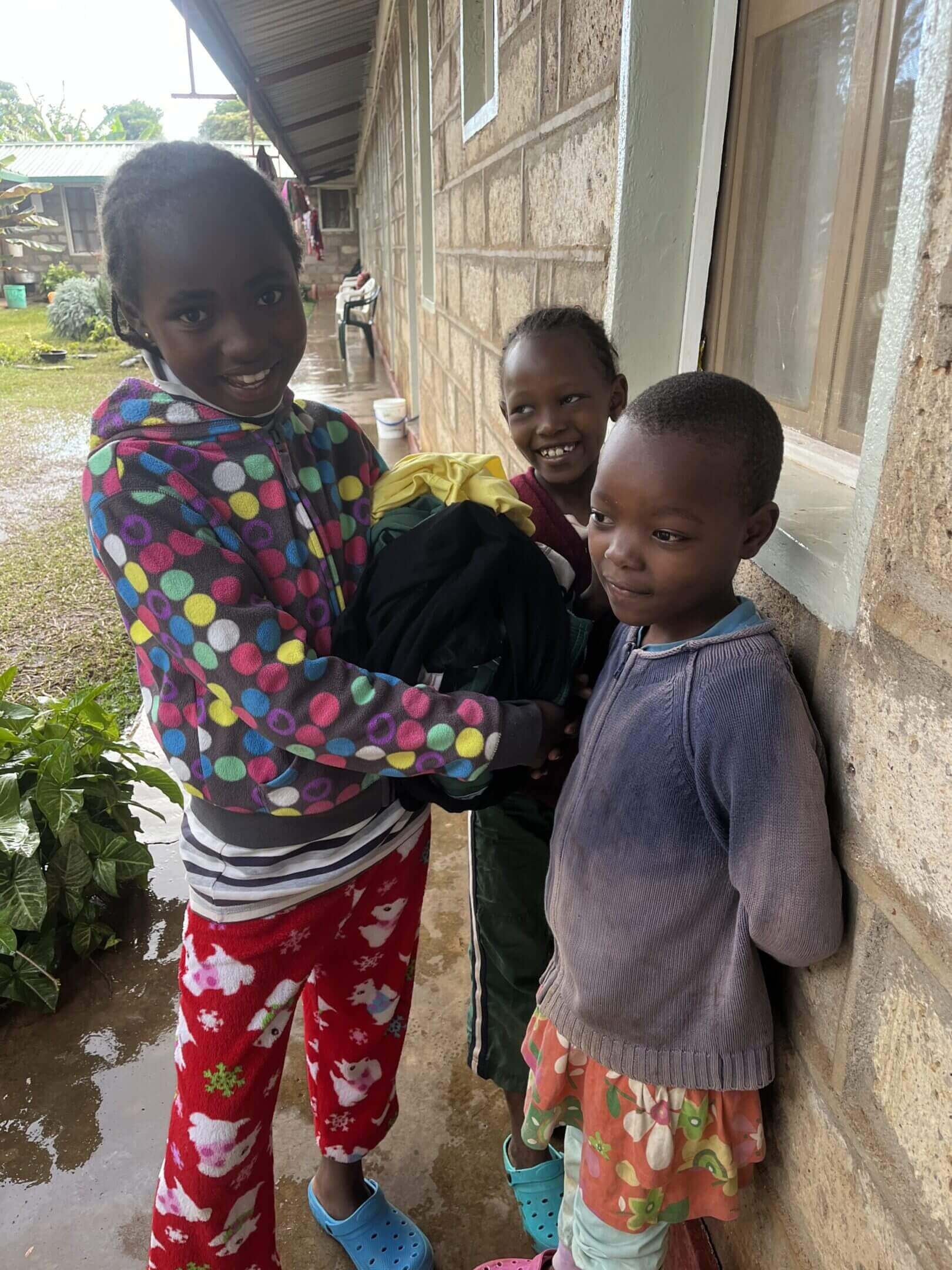 Three children smiling near a brick building.
